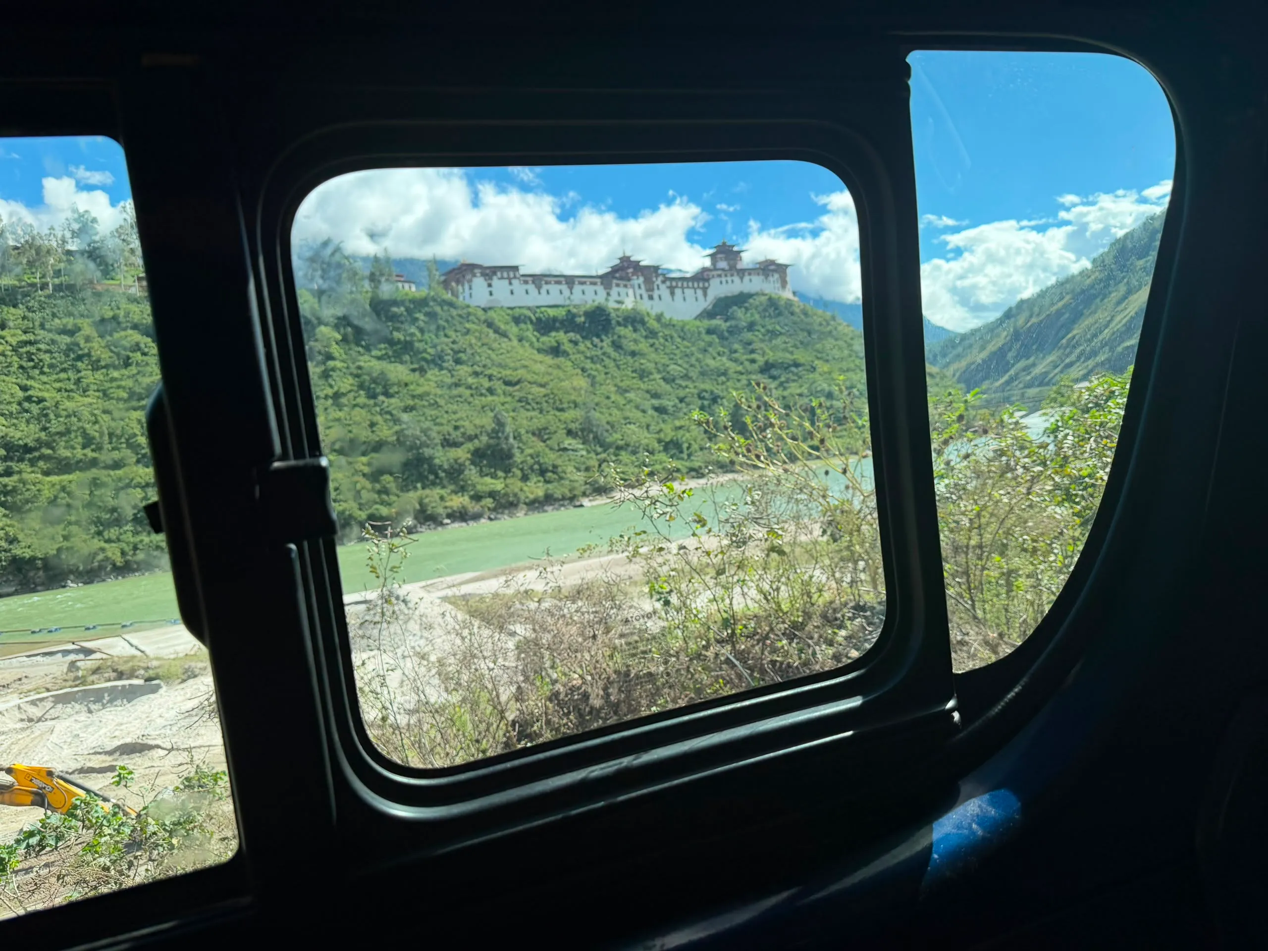 A hilltop dzong above a turquoise river seen through a travelling car window in Bhutan