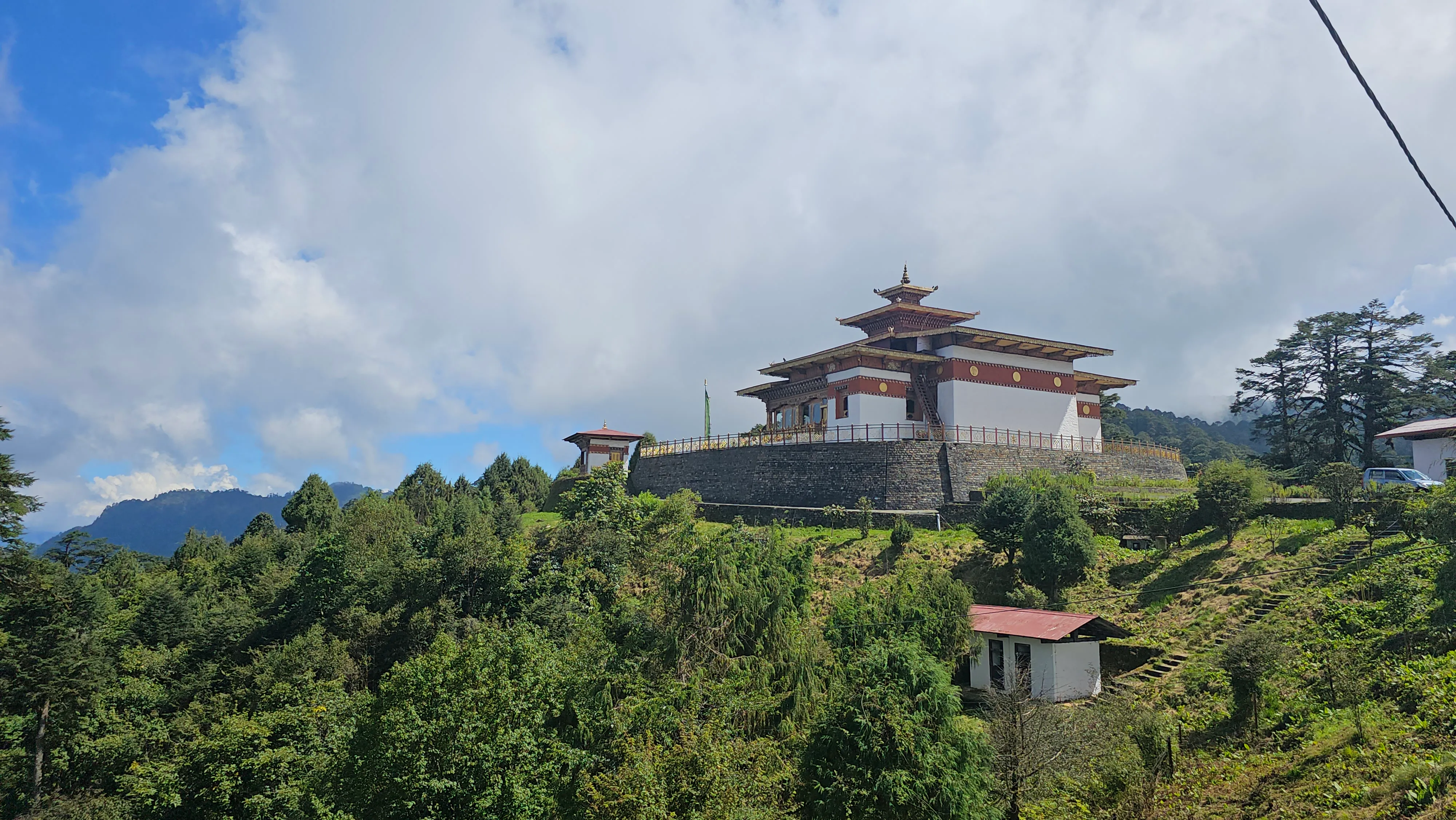 A hilltop lhakhang temple above forested slopes under a wide Bhutanese sky