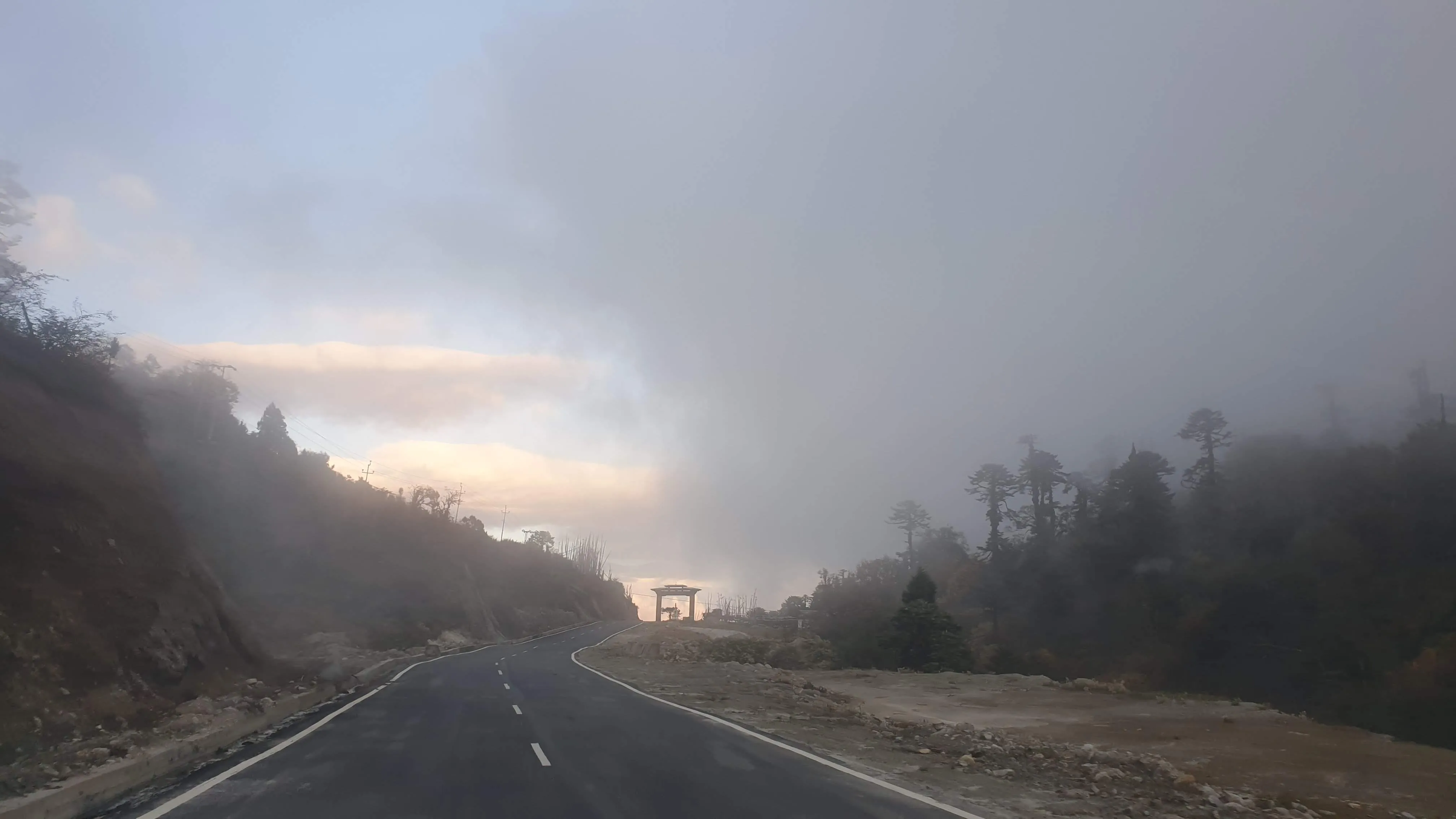 A misty Bhutanese mountain road curving toward a traditional gateway arch