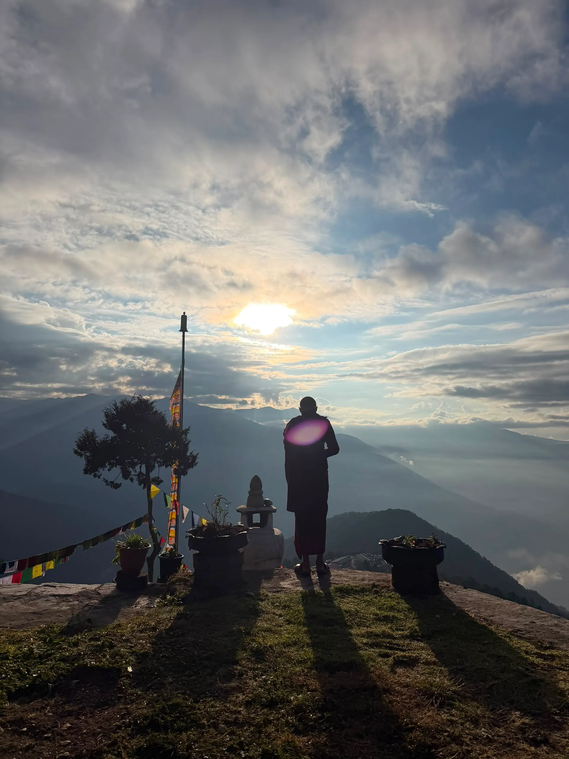 A monk on a mountaintop at dawn above the clouds with prayer flags