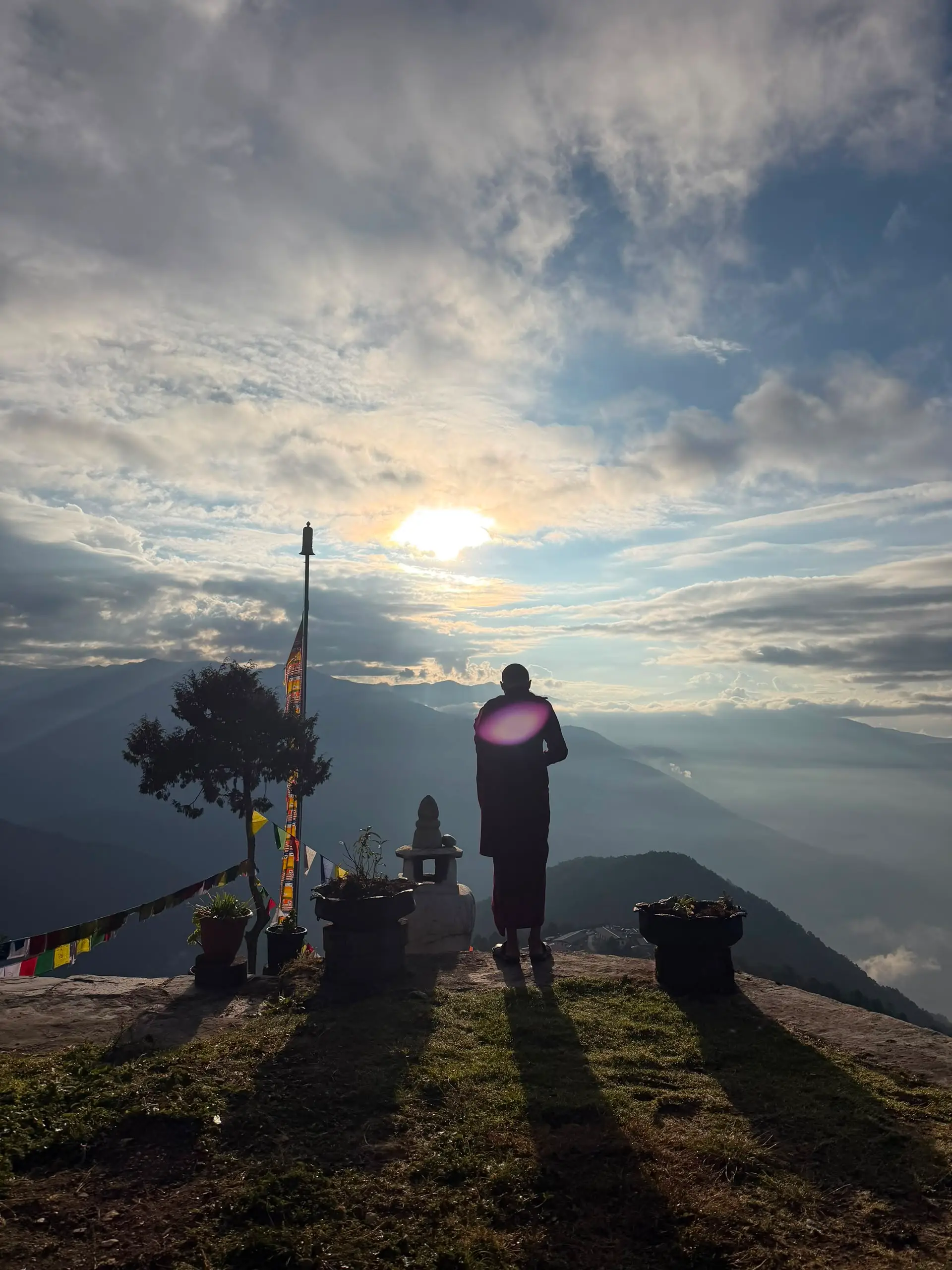 A monk on a mountaintop at dawn above the clouds with prayer flags