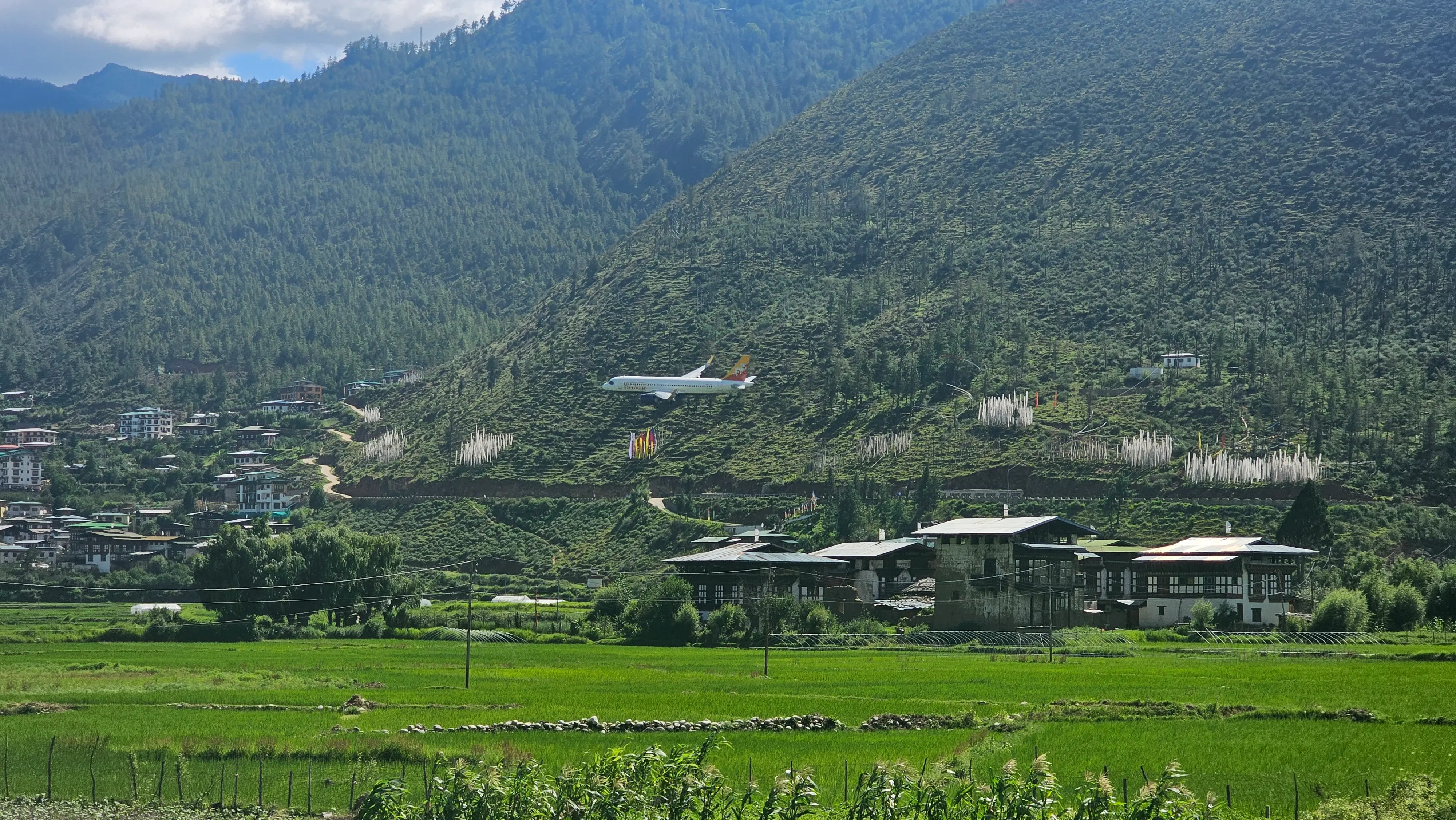 A Drukair jet on low final approach over the green Paro valley with farmhouses and rice fields