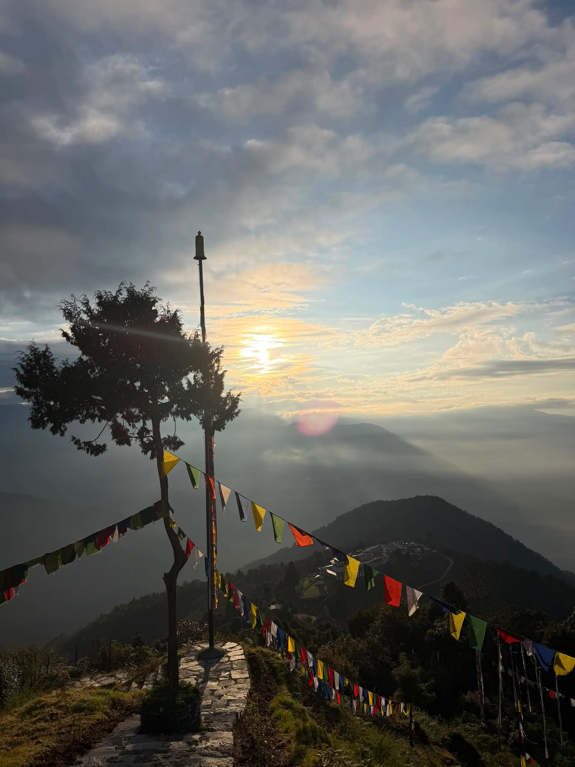 Sunrise over a ridge lined with colourful prayer flags above misty Bhutanese mountains