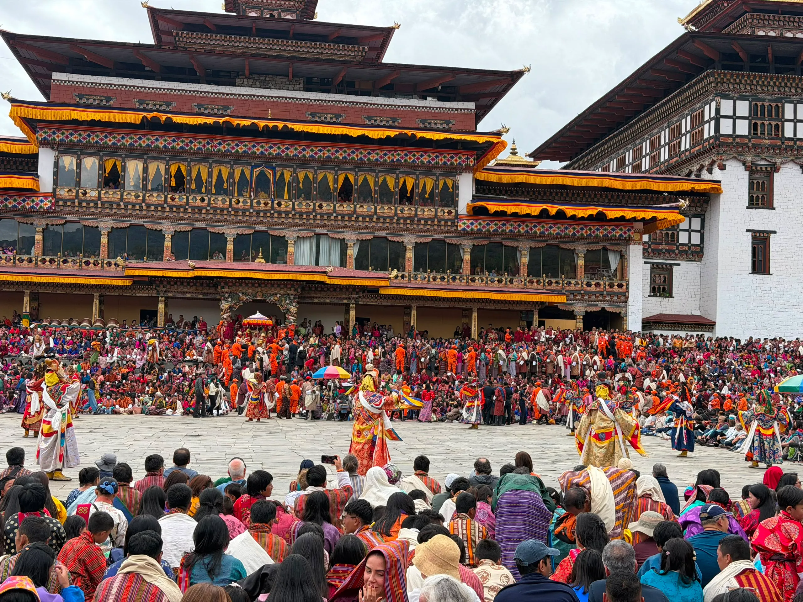 Masked cham dancers performing before a crowd in a Bhutanese dzong courtyard at a tshechu festival